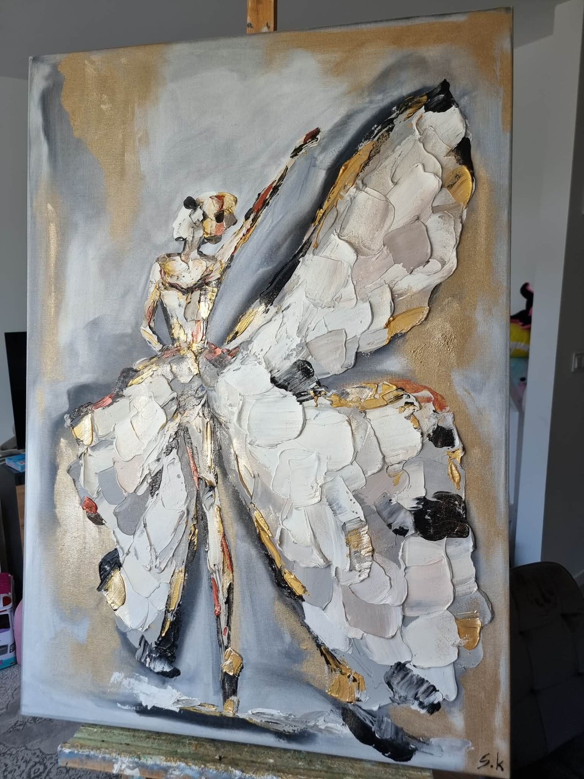 Abstract acrylic painting of a white butterfly with gold and gray accents on a tan canvas
