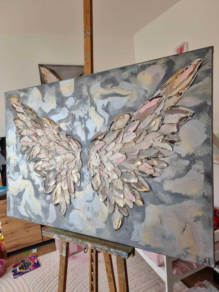 Painting of two detailed wings with pink and white feathers on gray and blue brushstroke background, displayed on easel in artists studio