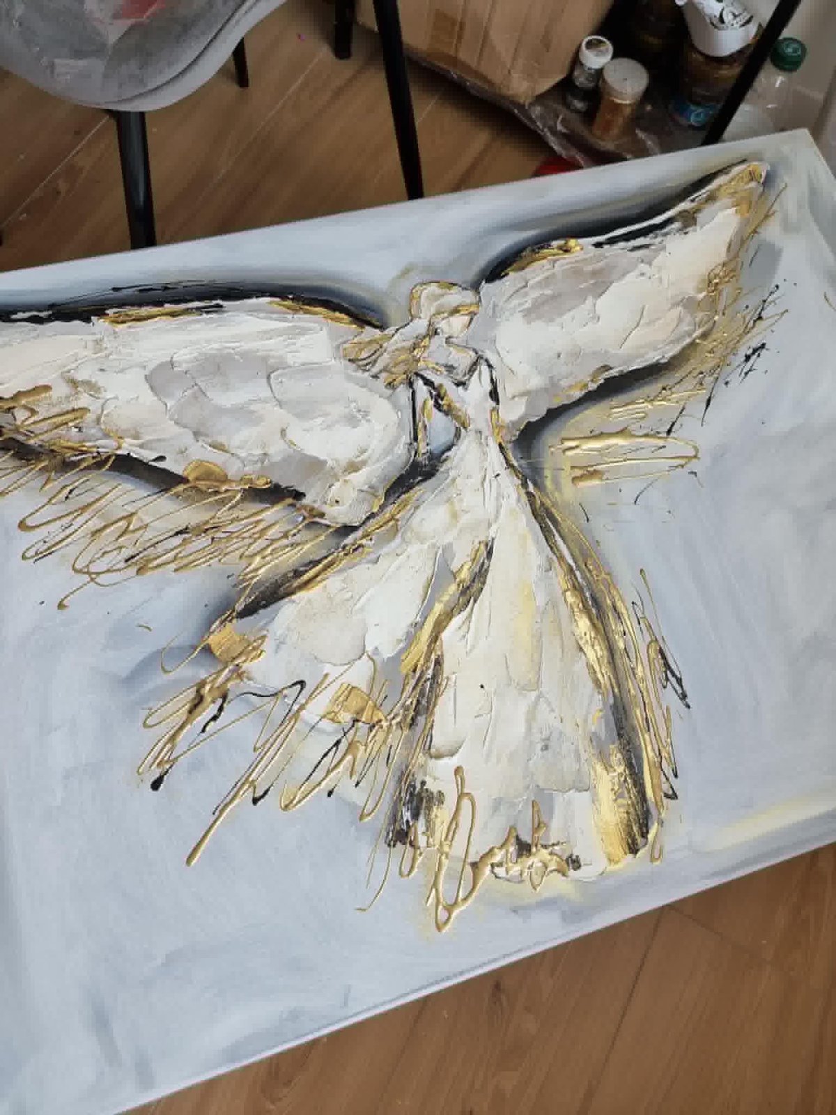 Textured white and gold acrylic painting of an angel or bird with outstretched wings on a white canvas in progress