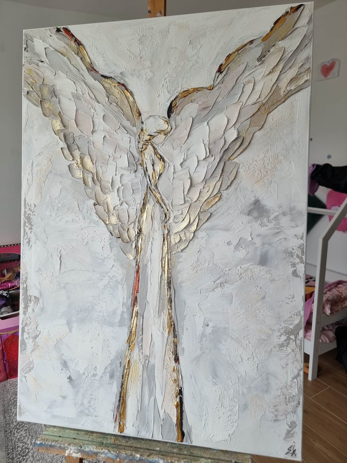 Textured abstract painting of an angel figure with white wings and gold accents on canvas in a room