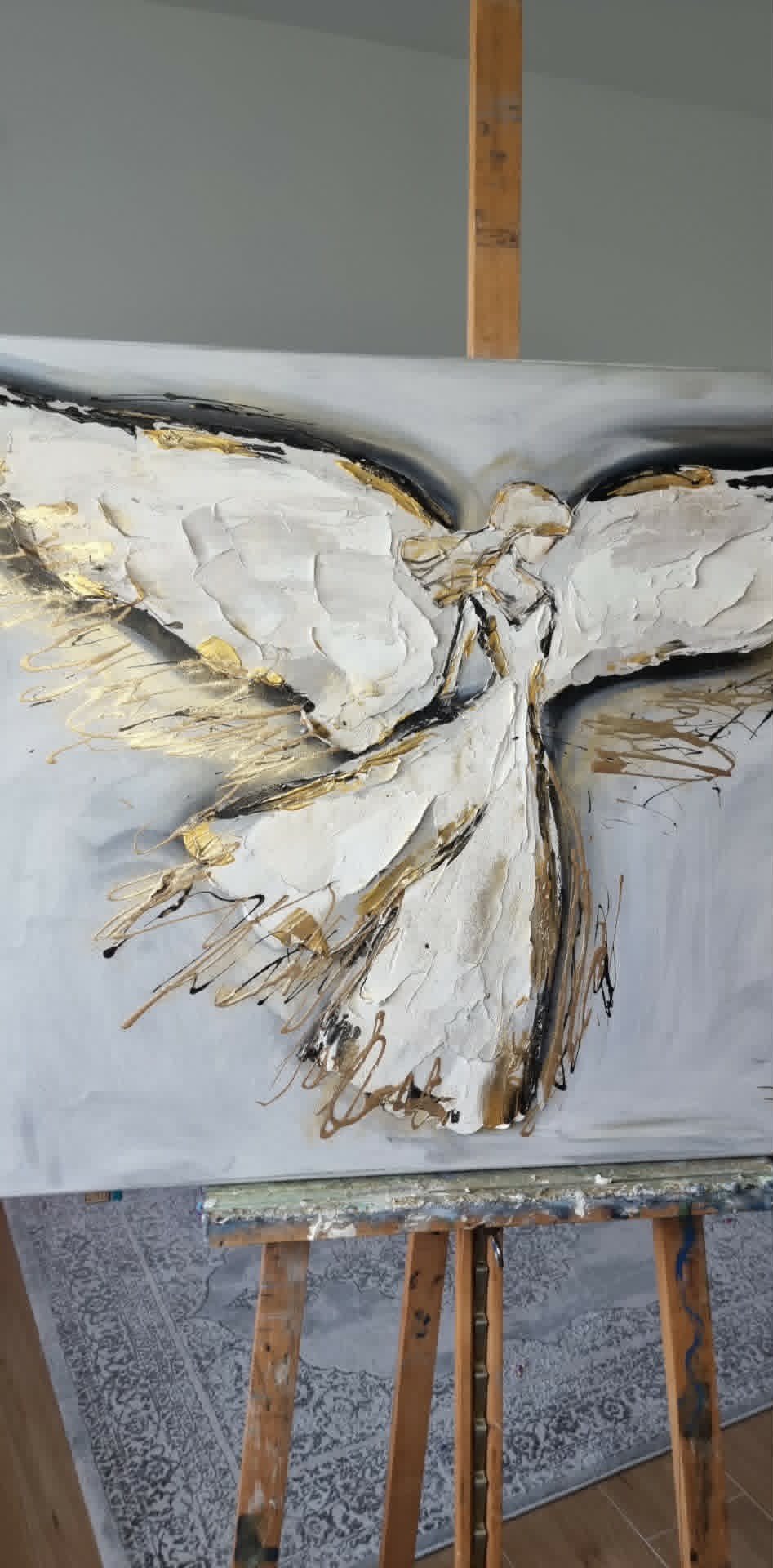 Abstract painting of a white and gold textured butterfly or bow on canvas, displayed on a wooden easel