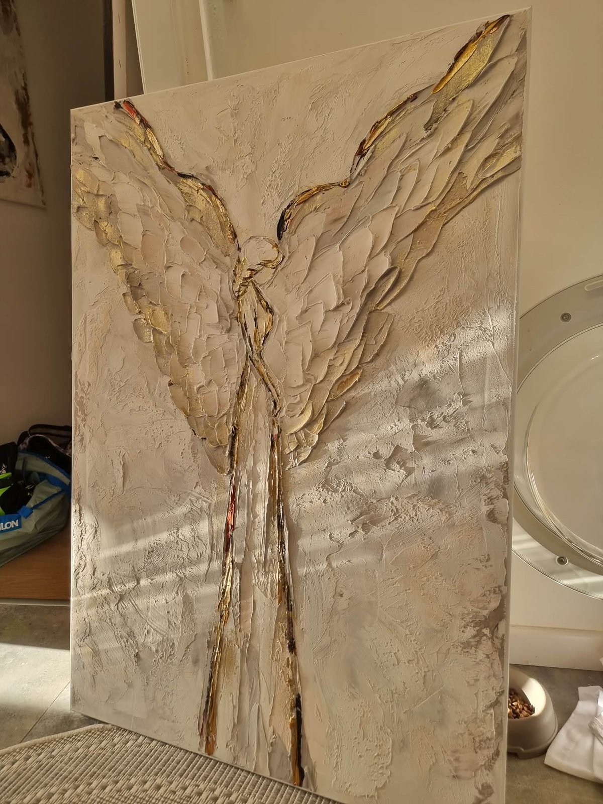 Textured canvas artwork depicting an angel figure with wings in cream and brown tones, displayed indoors