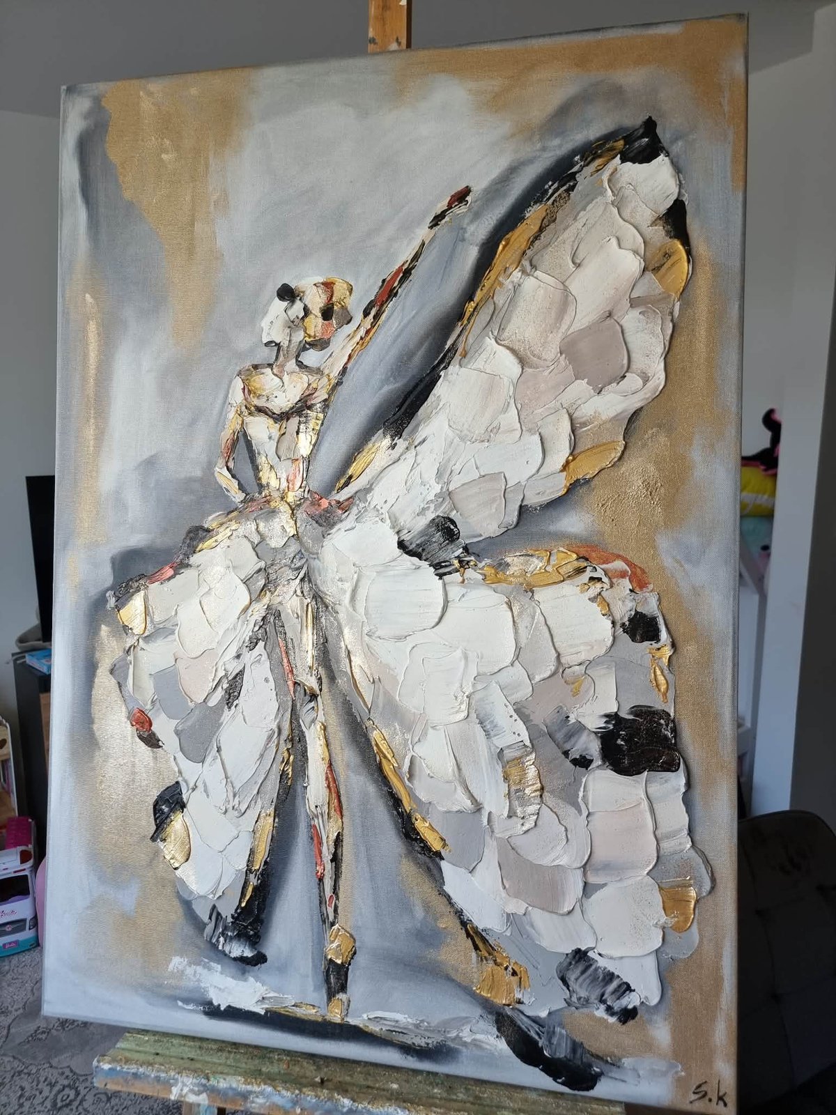 Abstract painting of a white butterfly with gold and black accents on a textured beige and gray background, displayed on canvas