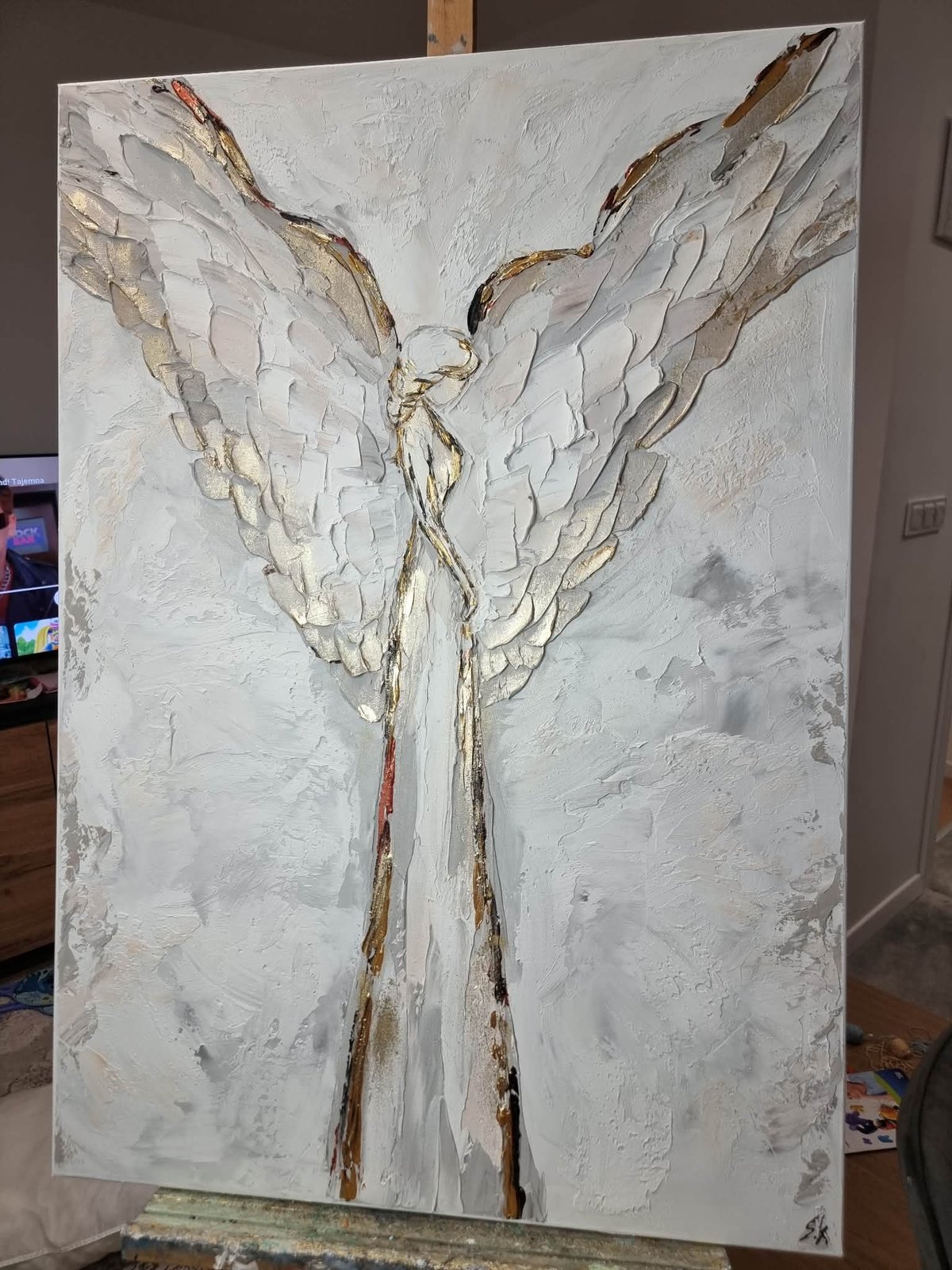 Abstract angel figure with white and gold textured wings on canvas, displayed in a home setting