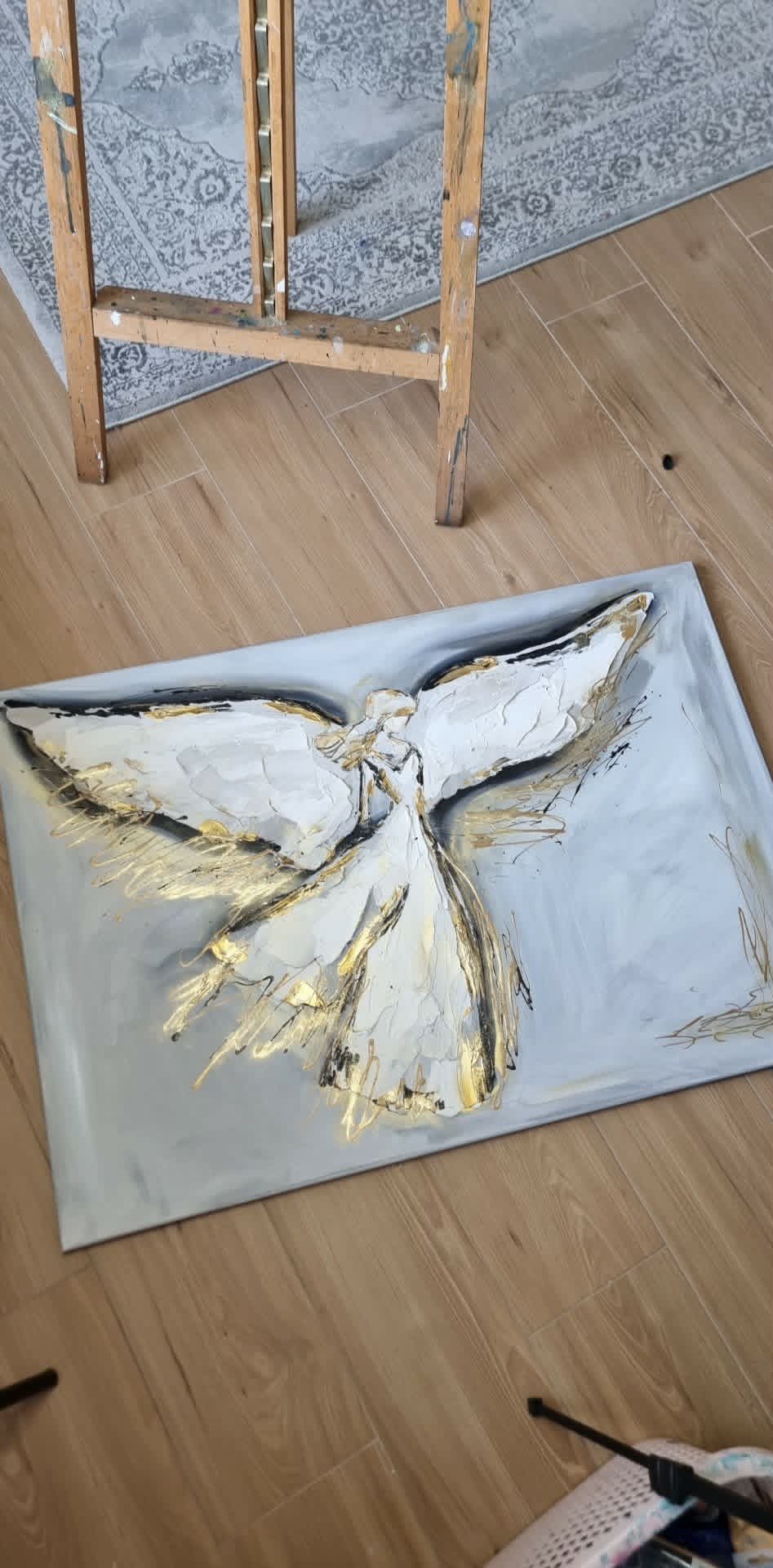 Textured abstract painting of an angel figure with white and gold brushstrokes on canvas on wooden floor